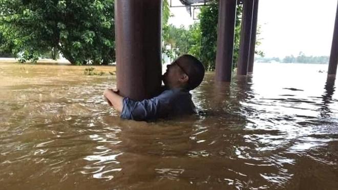 A man grips a post to avoid being swept away in floodwaters in Quang Binh province, Vietnam