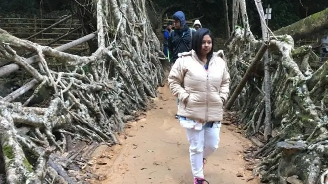 உயிர் வேர்ப் பாலத்தில் நடந்து வரும் ஒரு பெண் சுற்றுலாப் பயணி.