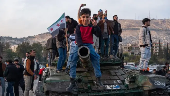 کودکی بر روی لوله تانک در دمشق. پرچم مخالفان سوری پشتش دیده می‌شود. عکس متعلق به امروز است