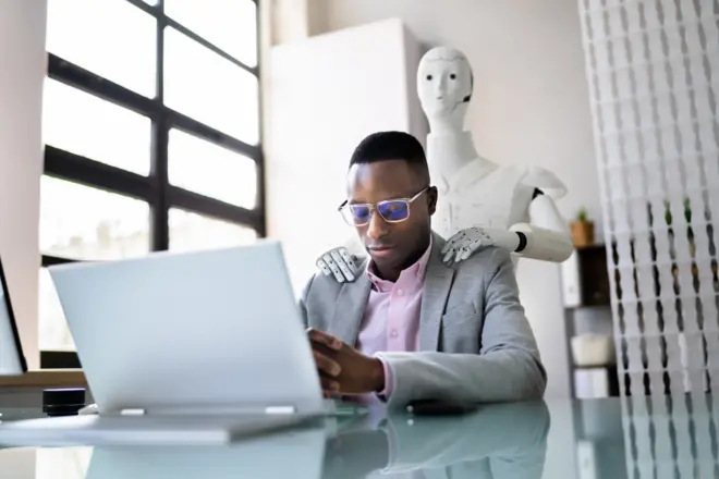 Un homme devant son ordinateur se fait tenir les épaules par un robot