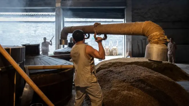 A worker connects two parts of steam vat filled with fermented grain in Chengdu, China