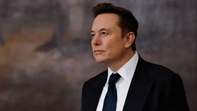 Elon Musk vestindo um terno preto, camisa branca e gravata preta olhando para longe
