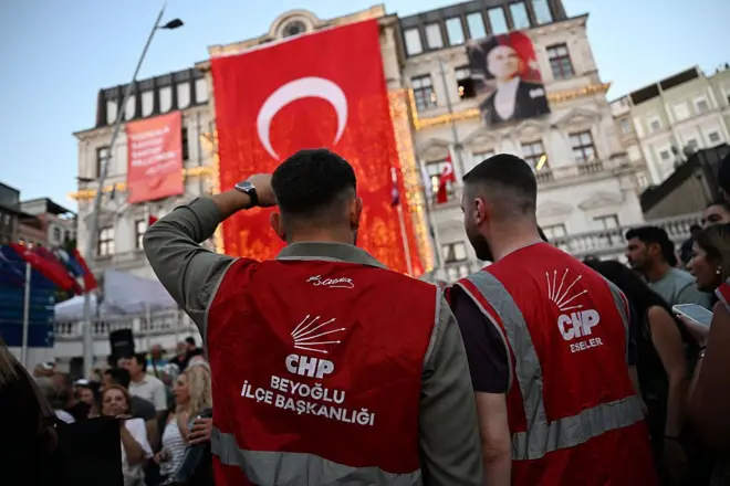 Üzerinde CHP Beyoğlu İlçe Başkanlığı yeleği olan iki erkek arkaları dönük bir şekilde Türk Bayrağına bakıyor. 