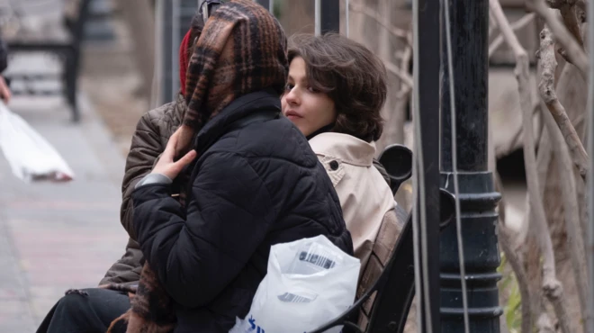 İkisi başörtülü biri başı açık üç kadın oturuyor. Başı açık olan genç kız kameraya bakıyor.