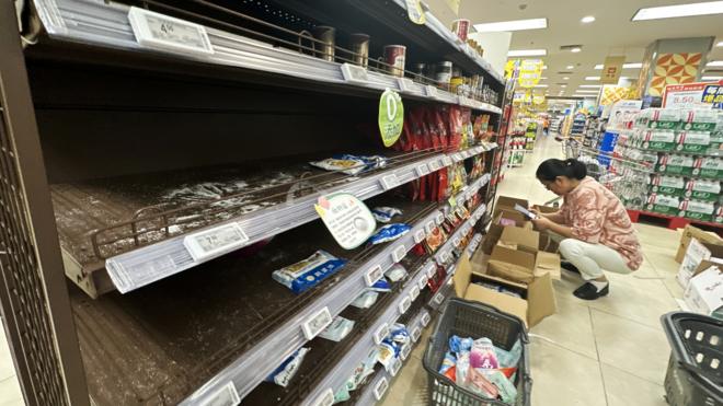重庆某超市一位女顾客在剩货无几的食盐货架底下选购（25/8/2023）