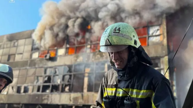Київ, велике полум'я підіймається з будівлі після російської атаки, на передньому плані стоїть рятувальник