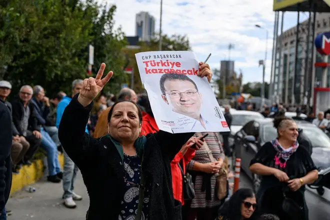İmamoğlu portresi taşıyan bir kadın barış işareti yapıyor, arkasında başka insanlar görülüyor