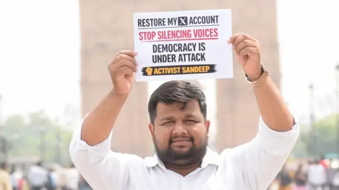 Sandeep Singh, an X user, holds up a placard saying 'Restore my X account. Stop silencing voices. Democracy under attack' on a street in India
