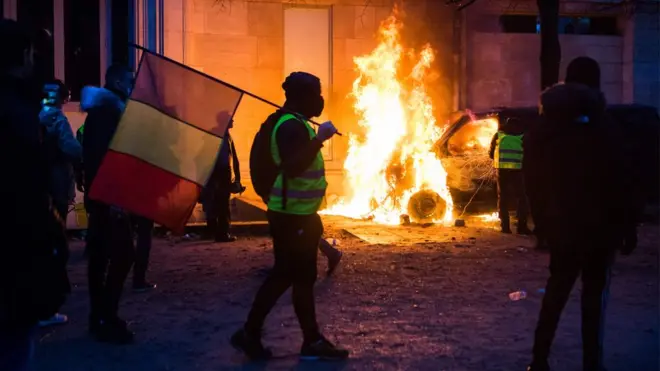 Протестувальник з прапором Франції біля палаючої машини