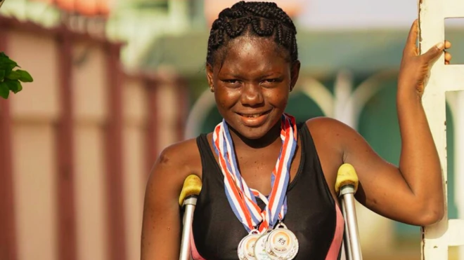 Regina hang medals for her neck, dey smile wit crutches under her arm