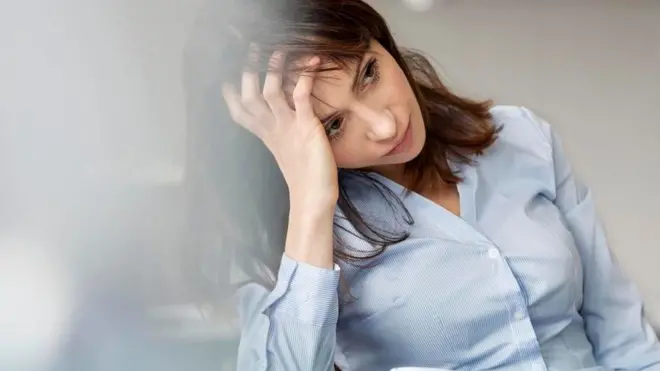 Una mujer con cara de agobio, apoyando la cabeza en una mano