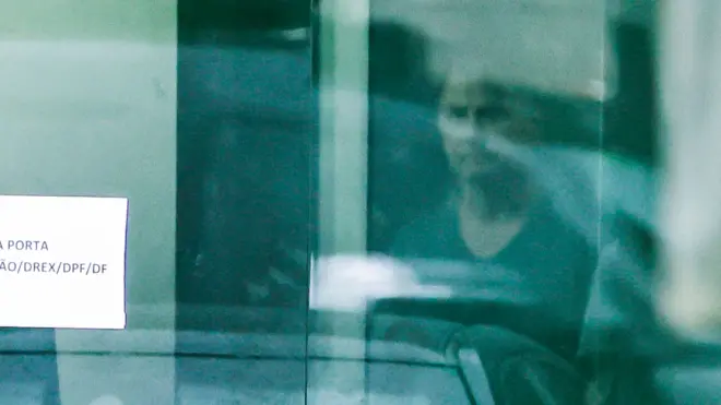 Jair Bolsonaro por trás da porta de vidro da Superintendência da Polícia Federal de Brasília neste domingo.