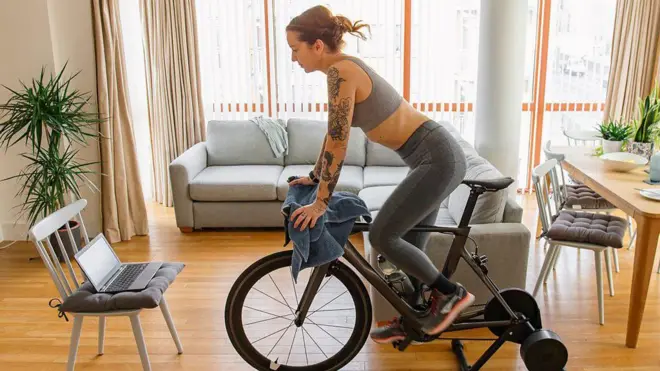 Mujer haciendo ejercicio en una bicicleta fija en la sala de la casa, vistiendo ropa deportiva