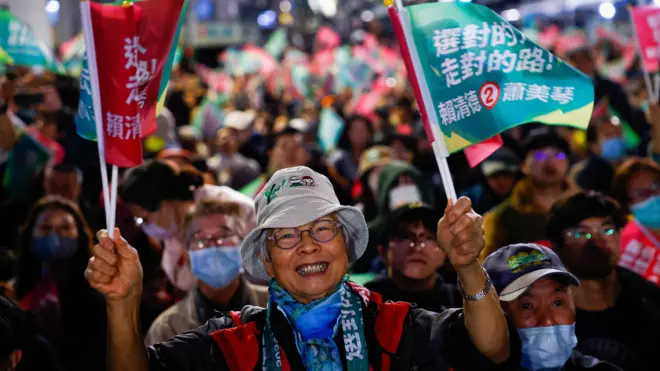 台灣民進黨台北開票集會上一位群眾揮舞小旗露齒而笑（13/1/2024）