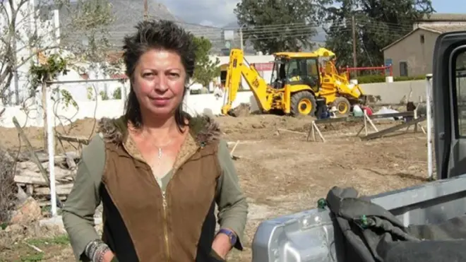 Uludağ, bir arazi aracının yanında duruyor, arkasında bir iş makinesi var, kameraya bakıyor, elleri ceplerinde. Tarihi bilinmiyor. 