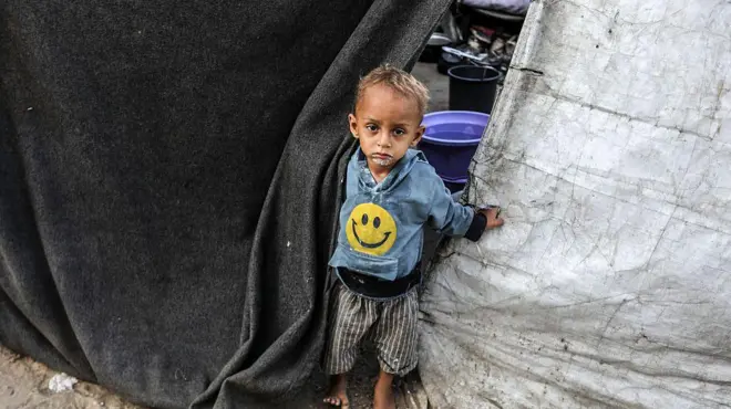 طفل صغيرينظر من وراء قماش احدى الخيام التي نصبتها عائلته فوق منزلها المهدم في خان يونس.