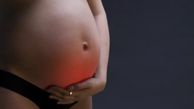 Caucasian pregnant woman in black lingerie with abdominal pain on gray studio background. Pregnancy concept with copy space