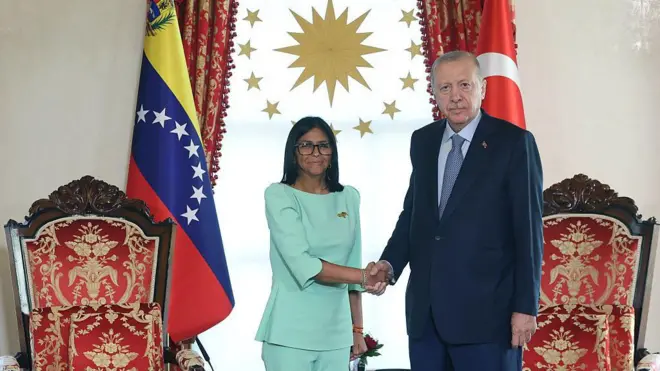 üzerinde açık mavi bir takım bulunan rodriguez (solda) Erdoğan ile el sıkışarak kameraya bakıyor