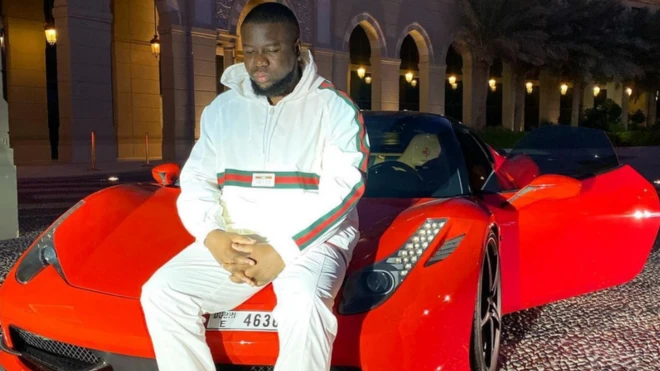 Hushpuppi assis sur une voiture rouge -photo postee sur Instagram