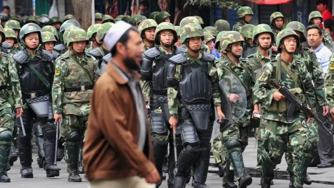 Хитой ҳарбийлари олдида бораётган уйғур эркак