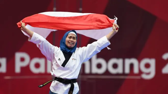Atlet taekwondo putri Indonesia, Defia Rosmaniar, berlari membawa bendera merah putih usai meraih medali emas pada partai final poomsae individu di Jakarta Convention Center (JCC), Minggu (19/8).