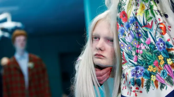 Close-up of female model in floral dress holding a mannequin head that is a replica of her head