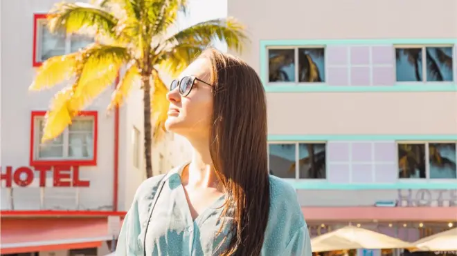Una joven mira al sol con un hotel de Miami Beach de fondo.