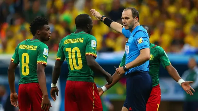 L'arbitre Jonas Eriksson parlant aux camerounais Benjamin Moukandjo et Vincent Aboubakar lors d'un match de Coupe du Monde 2014, opposant le Cameroun au Brésil dans le groupe A.
