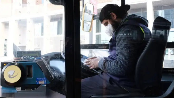 Motorista de ônibus em Londres sentado ao volante usando máscara e luva