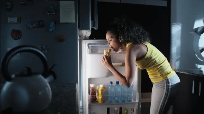 Une femme ouvre le frigo pour manger