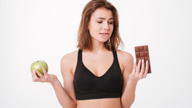 Mujer entre una manzana y una tableta de chocolate.