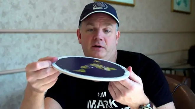 Un hombre sostiene una maqueta de la Tierra plana