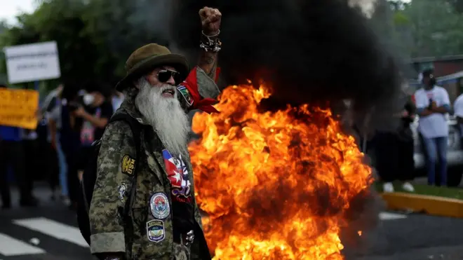 Protestor with raised hand and fire behind him