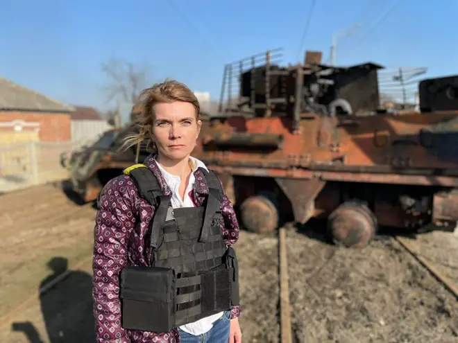 ผู้หญิงใส่ชุดกันกระสุนยืนหน้าซากรถถัง