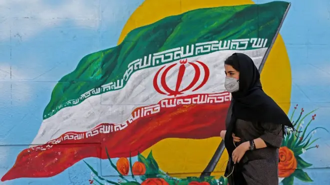 Iranian woman walks past mural