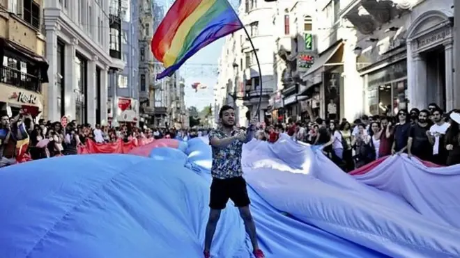 مردی در حال تکان دادن پرچم رنگین کمانی در جریان رژه افتخار ترنس‌ها در استانبول در ژوئن ۲۰۱۵.