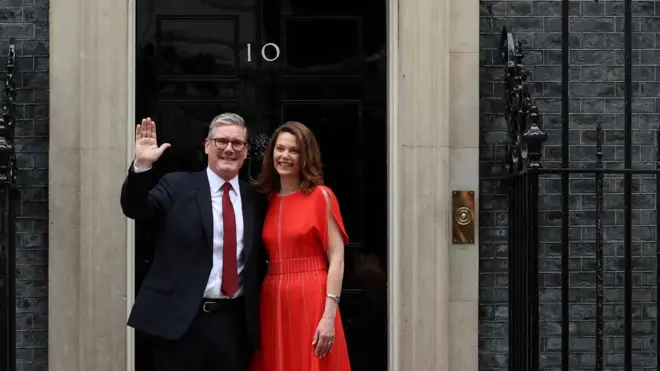施紀賢爵士(左)與夫人珺寧(Grinning Starmer;右)進入唐寧街10號前在正門向媒體記者揮手(5/7/2024)