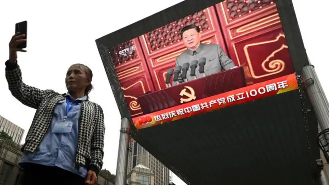 Seorang perempuan berfoto selfie dengan latar belakang tampilan Presiden China Xi Jinping saat pidato di Beijing.