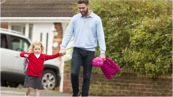 ወጣት አባት ሴት ልጁን ወደ ትምህርት ቤት ሲያደርስ