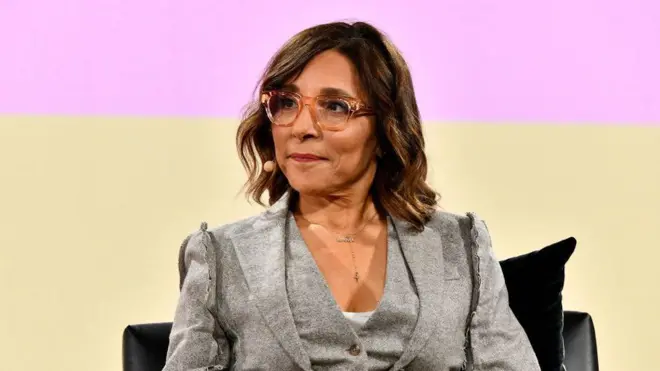 グレーのスーツにピンクの眼鏡をかけた女性がいすに座っている