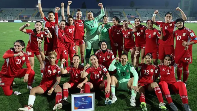 شادی بازیکنان تیم فوتبال زنان که پیراهن‌های سرخ پوشیده‌اند در زمین فوتبال