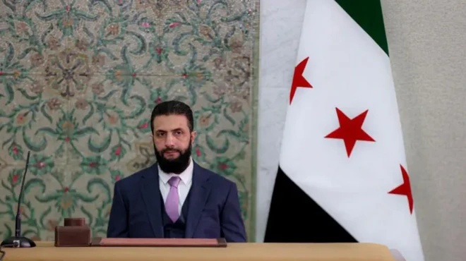 احمد شرع درکنار پرچم سوریه ایستاده است