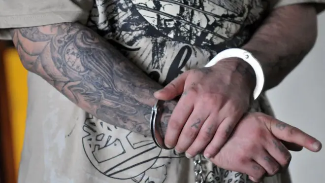 Carlos Reyes, también conocido como "Lobo", miembro de la pandilla "Mara 18", realiza gestos mientras es escoltado a la corte en Ciudad de Guatemala el 24 de agosto de 2010. Trece miembros de la pandilla enfrentan acusaciones de extorsión y asesinato de pilotos. (Foto de JOHAN ORDONEZ/AFP vía Getty Images)