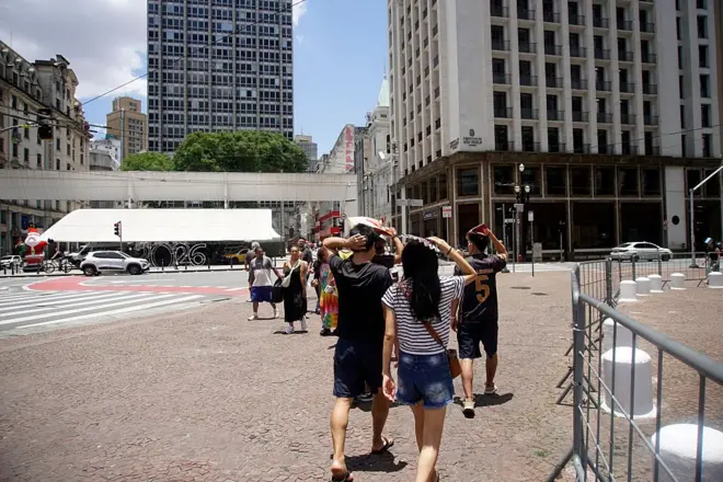 Pedestres se protegem do calor na região central da cidade de São Paulo, Brasil, em 29 de dezembro de 2025, enquanto um termômetro de rua registra 34°C.