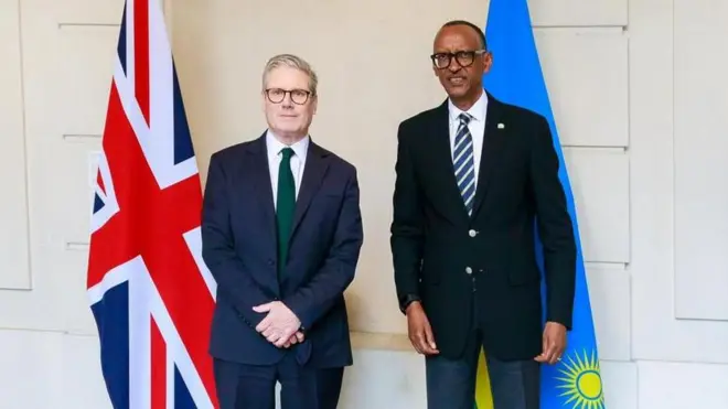 Perezida Paul Kagame na Minisitiri w'intebe w'Ubwongereza Sir Keir Starmer ubwo bahuriraga i Paris mu Bufaransa mu mikino Olempike yo mu mpeshyi ya 2024. Bambaye kositimu na karuvati, bahagaze iruhande rw'ibendera ry'Ubwongereza n'ibendera ry'u Rwanda.