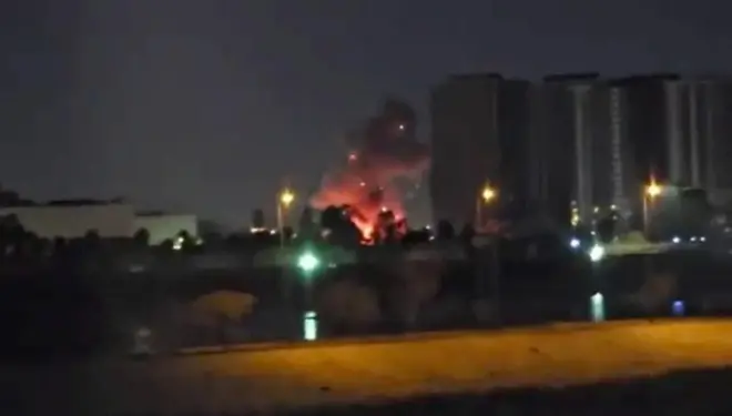 動画から切り出した静止画。夜の暗闇の遠方に、火事の炎と黒い煙が大きく立ち上っている。周囲には街灯や高層ビル群も映っている