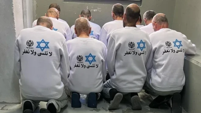 سجناء فلسطينيون يرتدون قمصاناً تحمل شعار مصلحة السجون الإسرائيلية وعبارة "لن نغفر ولن ننسى"، نشرتها مصلحة السجون يوم السبت