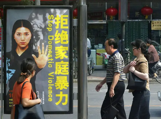 街头上一幅印有“拒绝家庭暴力”的海报，三名途人经过。