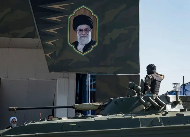 يؤدي جندي إيراني التحية العسكرية أثناء نقله على متن دبابة عسكرية أمام صورة المرشد الأعلى الإيراني، آية الله علي خامنئي، خلال عرض عسكري بمناسبة ذكرى يوم الجيش 2025
