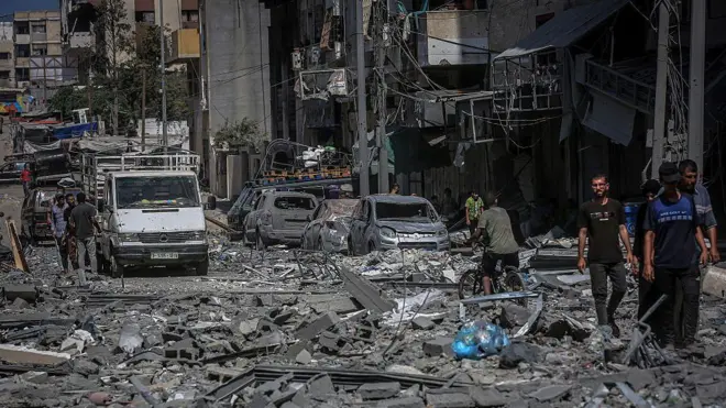 በፍንዳታ የተጎዳ ሕንጻ እና መኪኖች የሚታዩበት በፍርስራሽ የተሸፈነው የጋዛ ከተማ ሪማል አካባቢ መንገድ